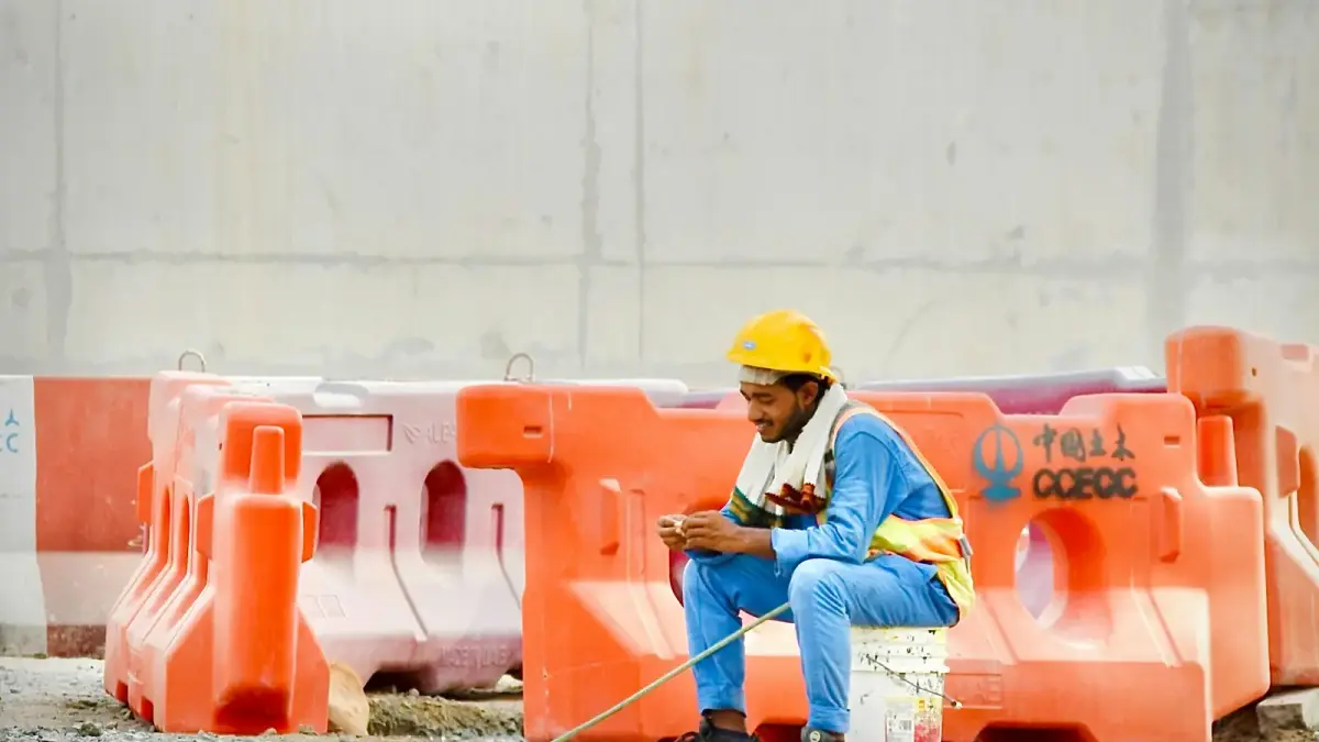 Construction worker in hard hat sits on bucket using phone.