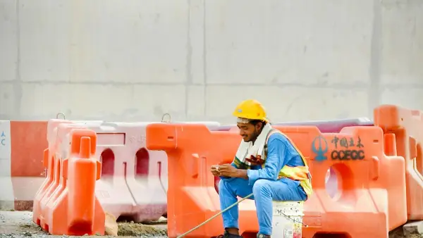 Construction worker in hard hat sits on bucket using phone.