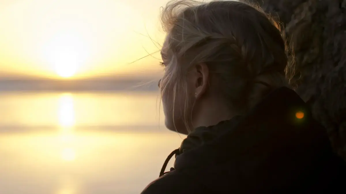 woman in black hoodie staring at the sea at sunset
