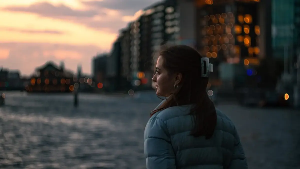 Woman looking out at a city waterfront at dusk