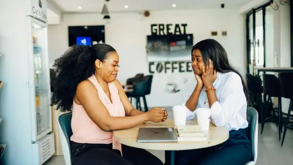 A couple of women sitting at a table with a laptop