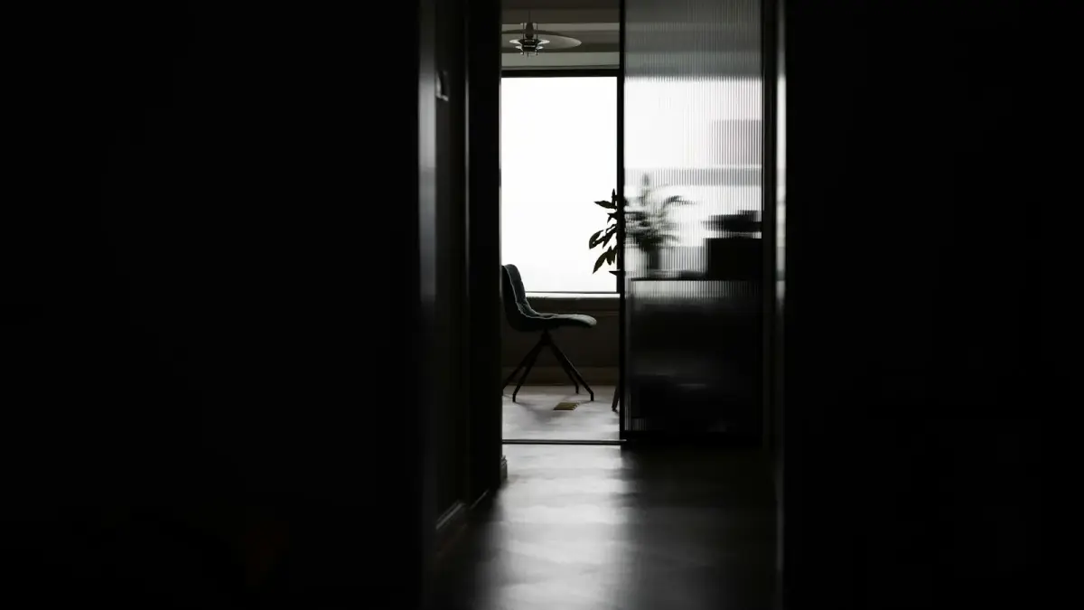 Dark hallway leading to a bright room with a chair