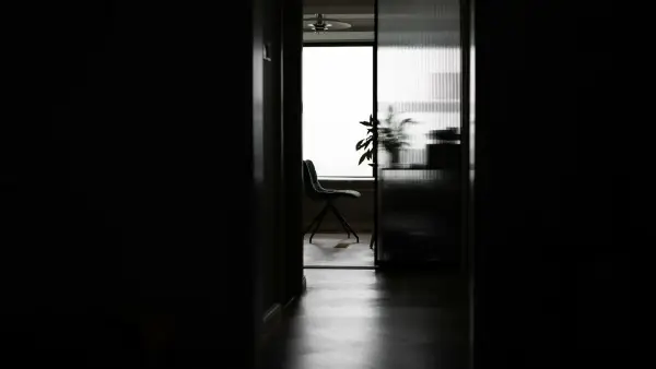 Dark hallway leading to a bright room with a chair