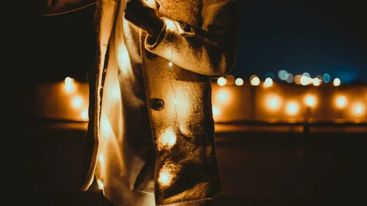 person in gray coat holding string light