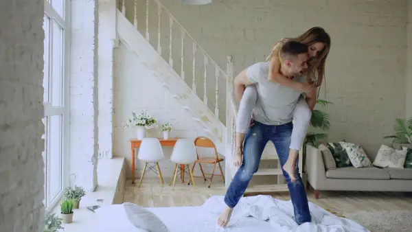 Couple piggybacking on a bed in a bright room
