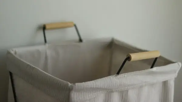 An empty, light-colored laundry hamper with wooden handles.