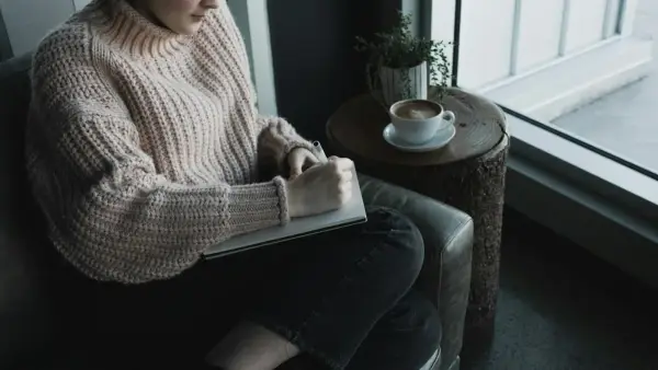 woman in white knit sweater and blue denim jeans sitting on gray sofa chair reading book