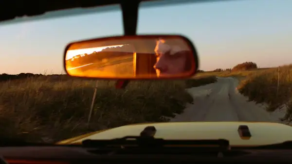 a car's view of a dirt road in the rear view mirror