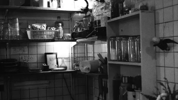 A cluttered kitchen shelf with jars and utensils.