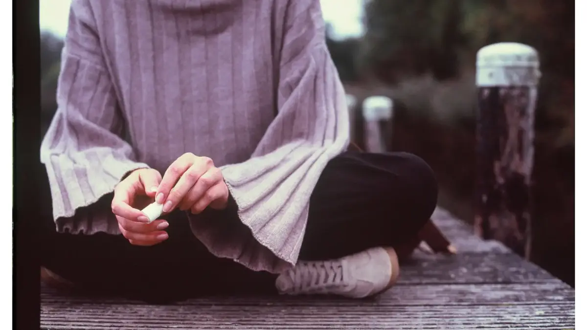 Person sitting on a wooden dock with hands clasped.