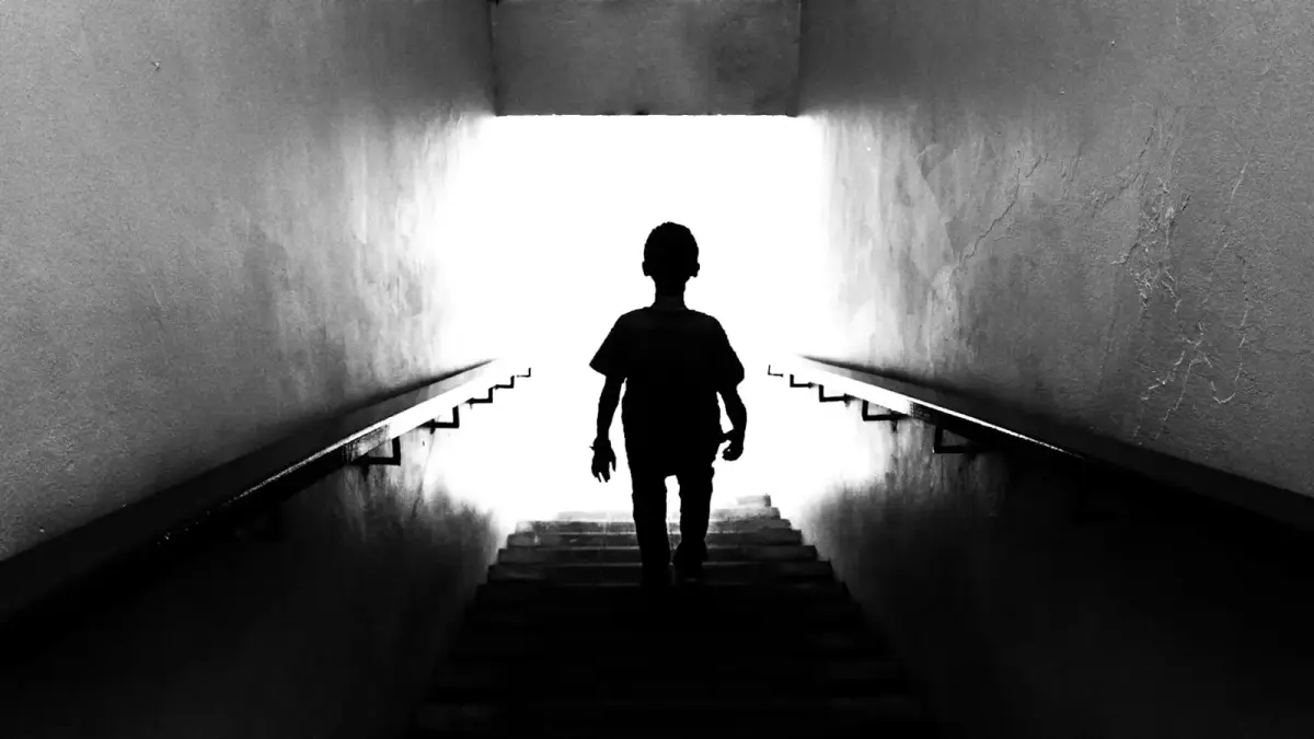 Silhouette of a child walking up stairs towards light.