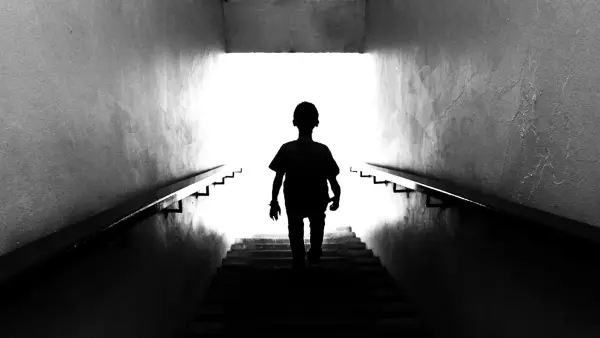 Silhouette of a child walking up stairs towards light.