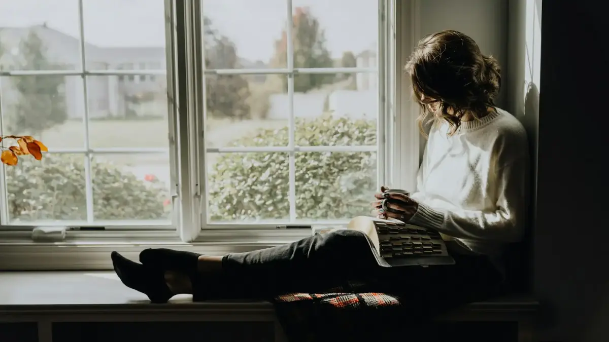 A woman sitting on a window sill reading a book