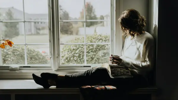 A woman sitting on a window sill reading a book