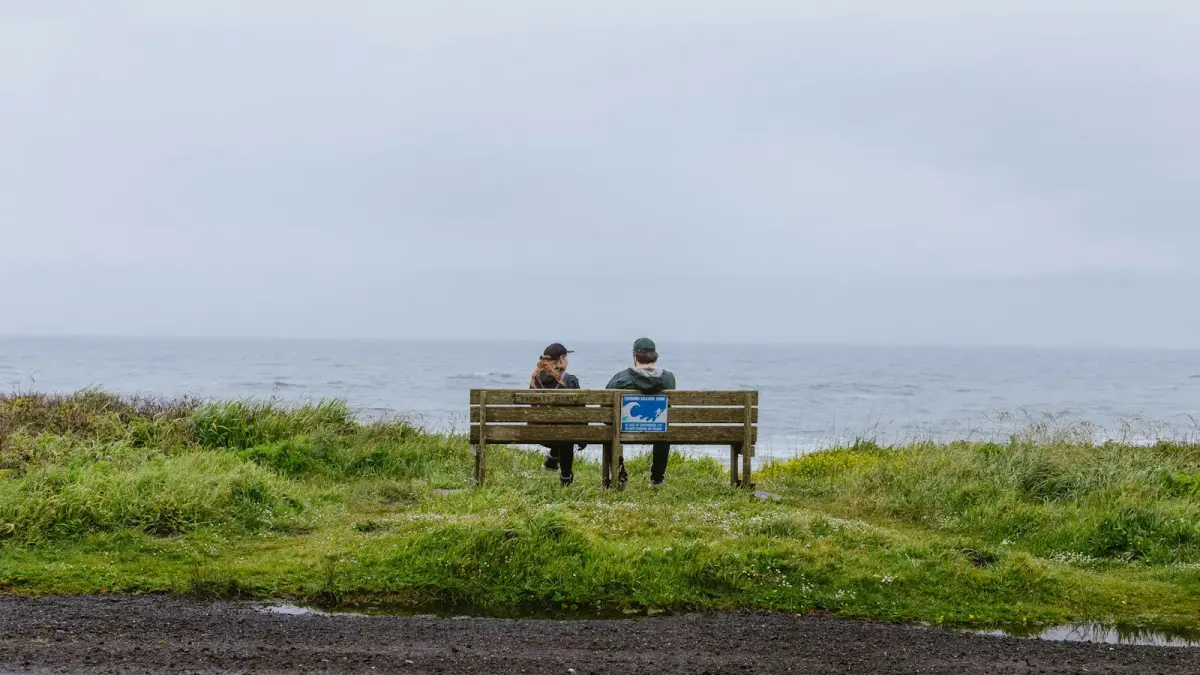 two people sitting on a bench near the ocean