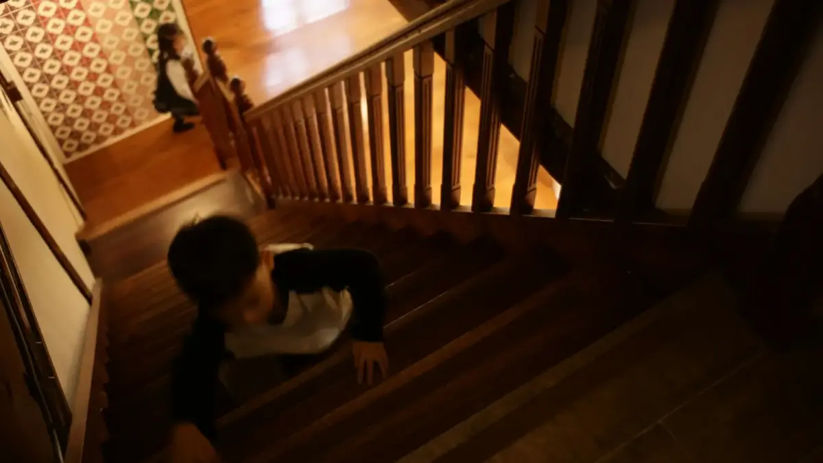 A boy crawls up wooden stairs while a girl watches.