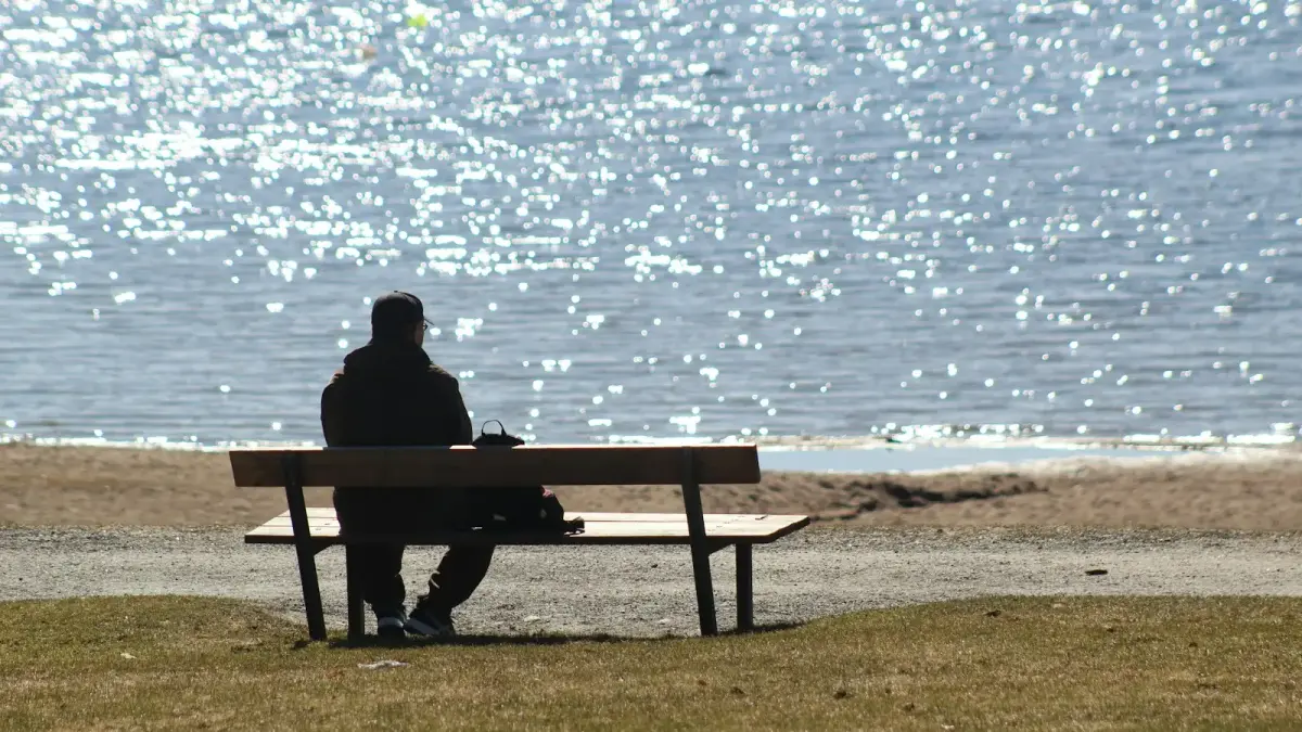 man sitting on bench near sea during daytime