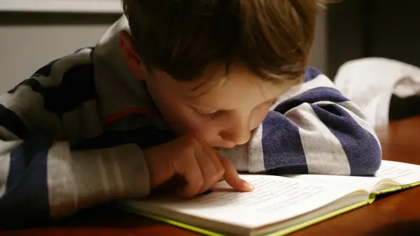 A child in a striped shirt reading a book at a wooden table