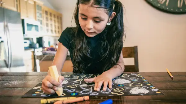 a young girl sitting at a table drawing with crayons