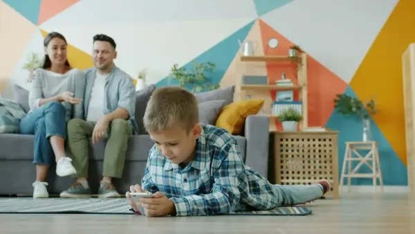 Boy plays on phone while parents watch from couch