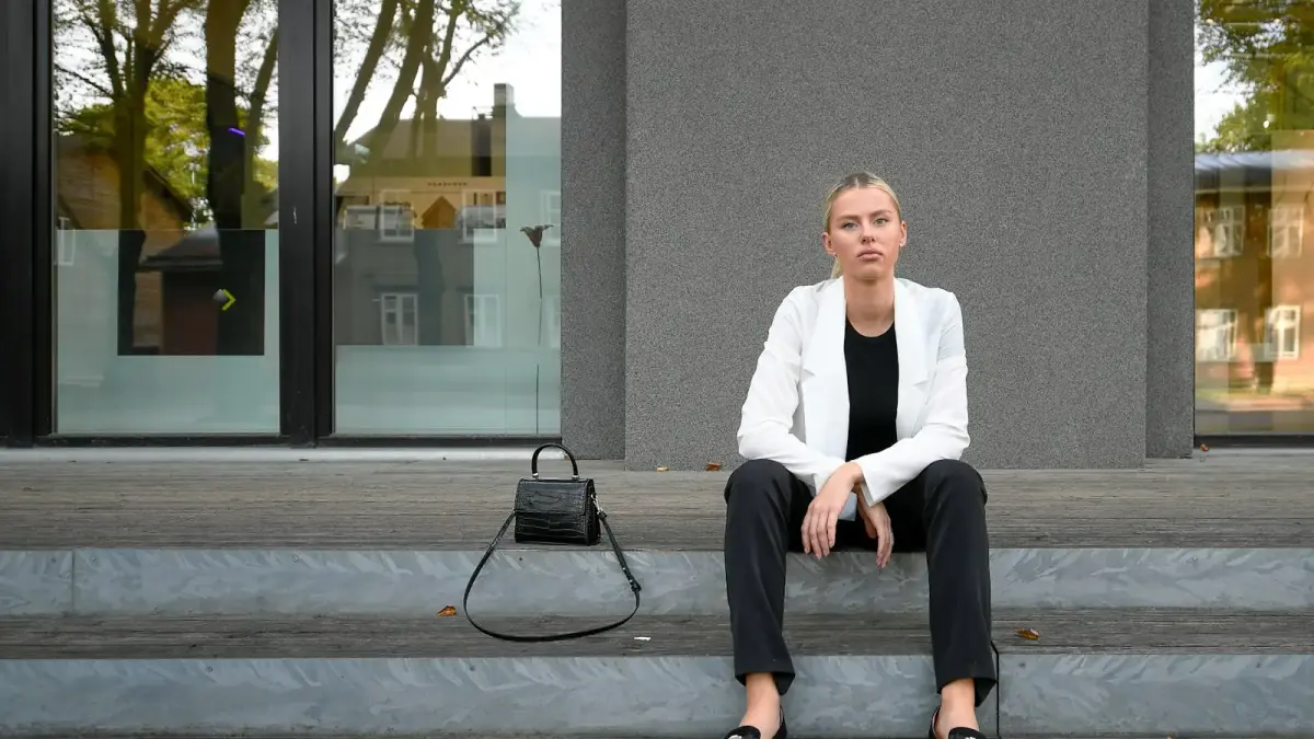 A woman in a white blazer sits on building steps.