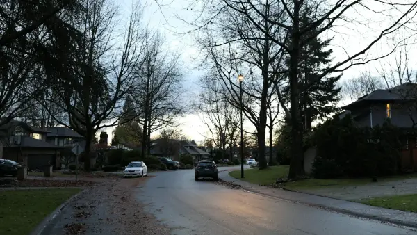 Cars driving on a wet suburban street at dusk.