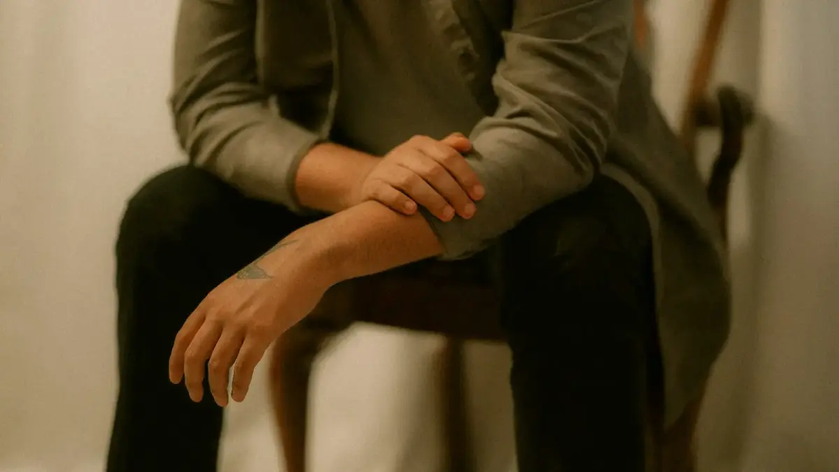 A person sits on a chair with arms crossed.