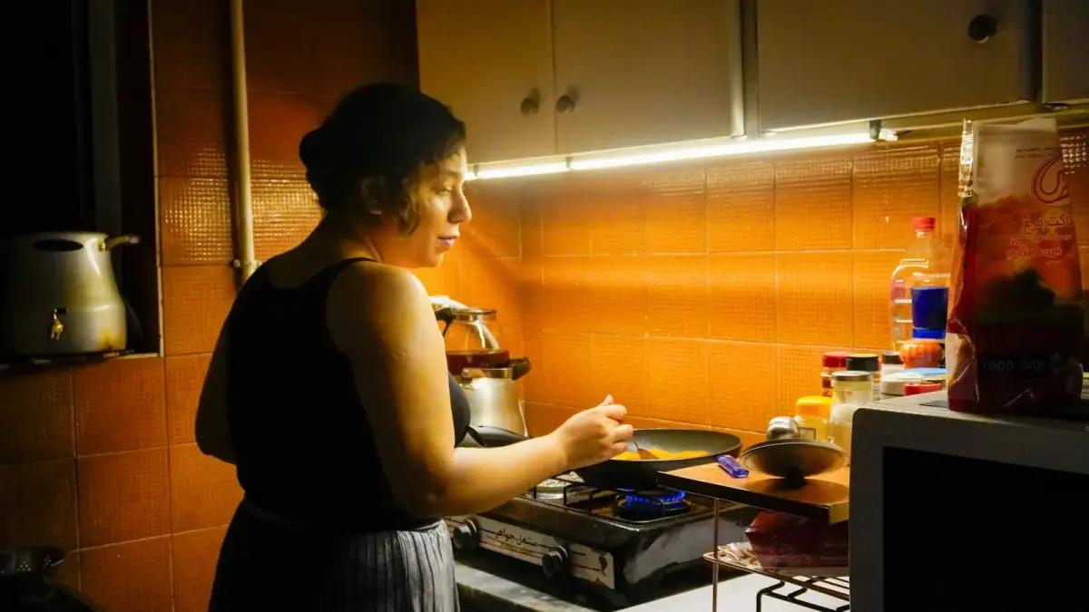A woman cooks food in a small kitchen.