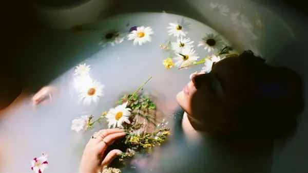 woman sitting in bathtub with white and yellow daisy flowers