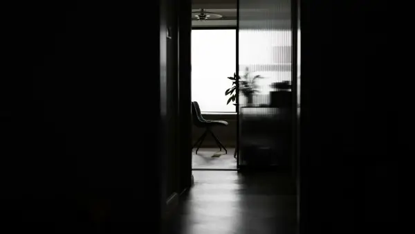 Dark hallway leading to a bright room with a chair.
