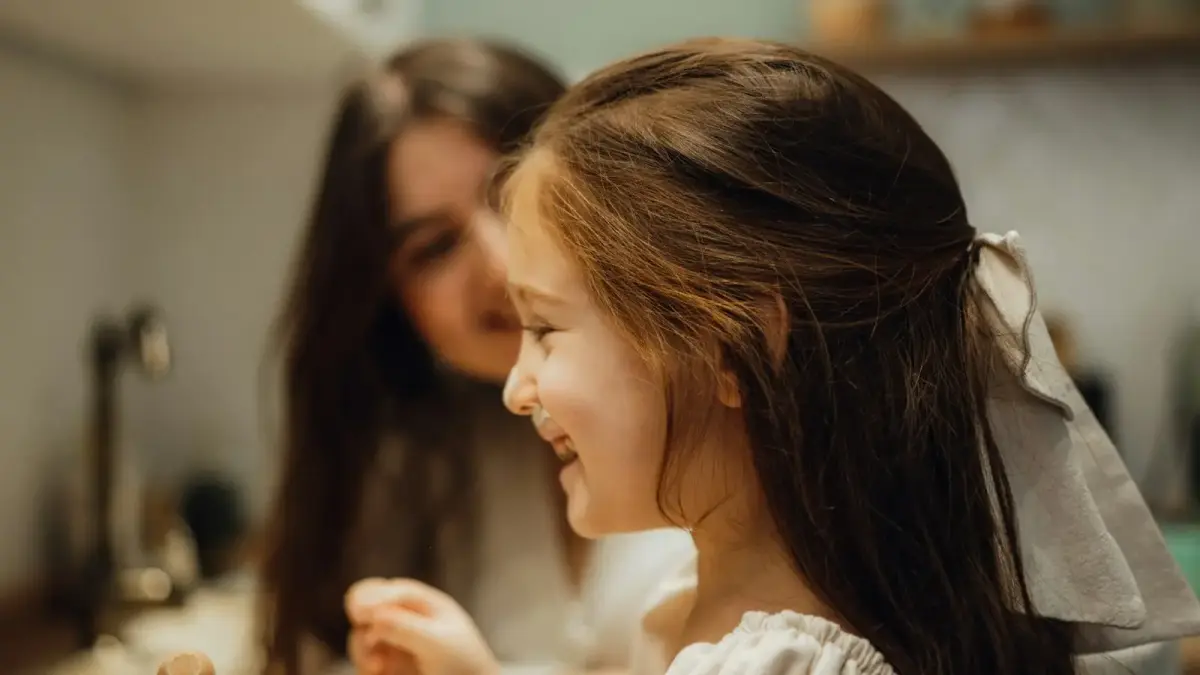 A little girl sitting in front of a sink next to a woman