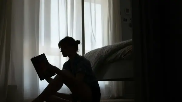 man in blue t-shirt sitting on bed reading book