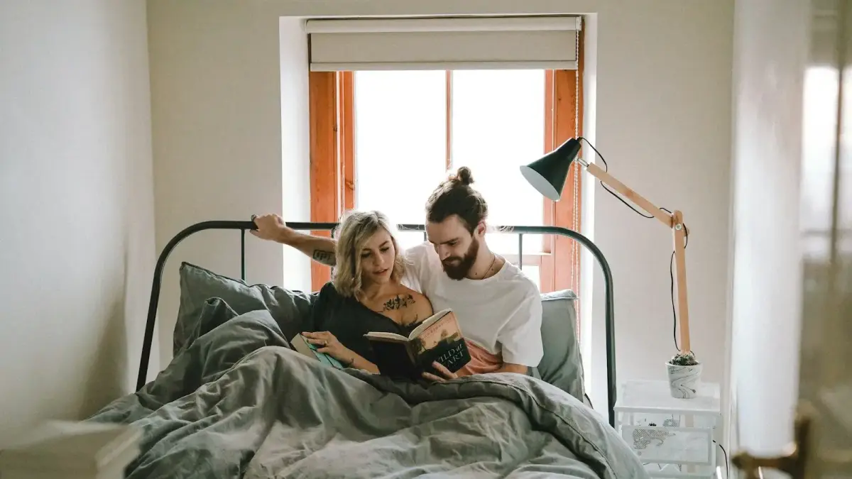 man and woman reading book on bed