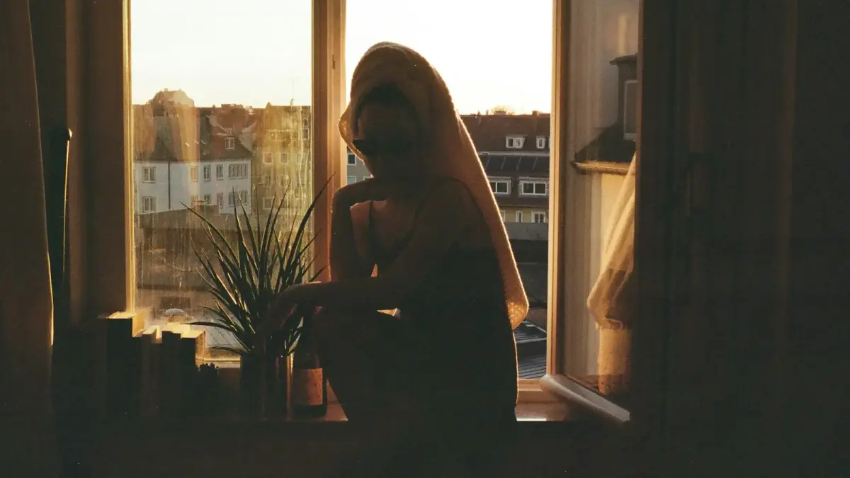 a woman standing in front of a window next to a potted plant