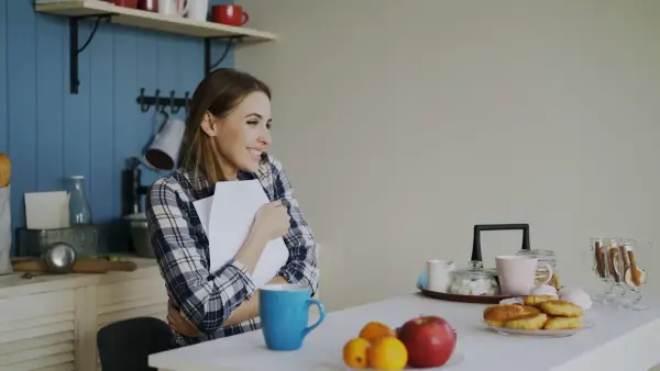 Woman holding book at kitchen table with snacks.
