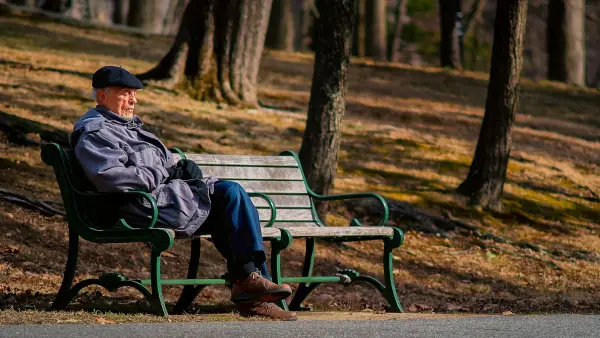 man in black jacket sitting on brown wooden bench