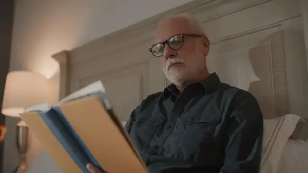 Senior man with glasses reading documents in bed.