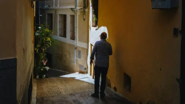 Man walking in a narrow, sunlit alleyway.