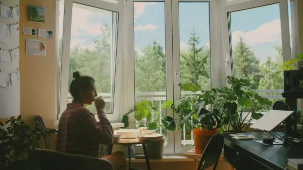 A woman drinking from a mug at a table by a sunlit window