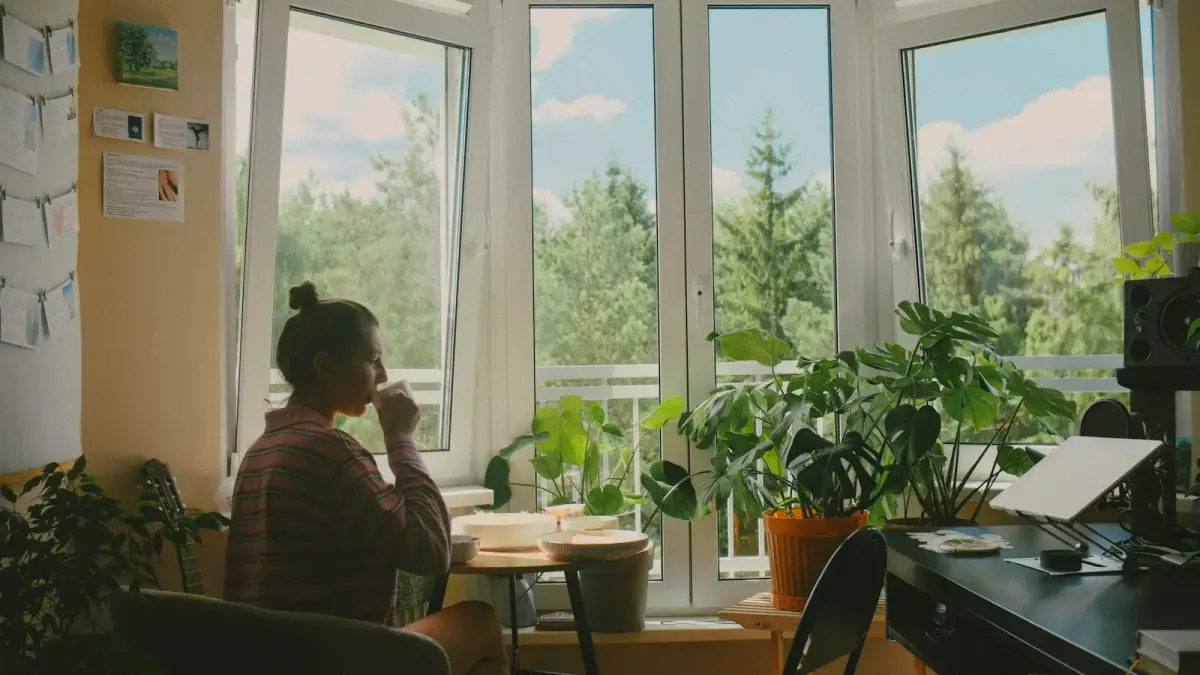 A woman drinking from a mug at a table by a sunlit window