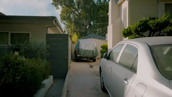 A car parked in a narrow driveway between houses.