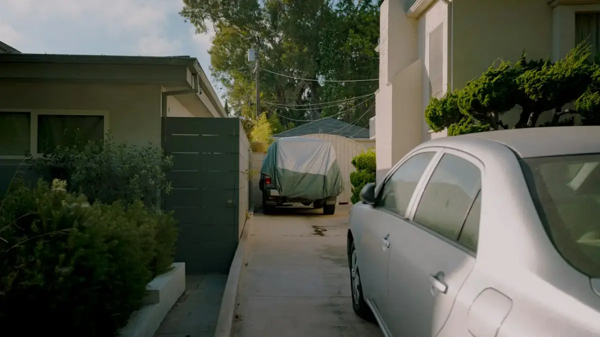 A car parked in a narrow driveway between houses.