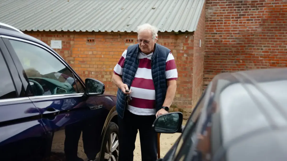 An older man stands between two cars