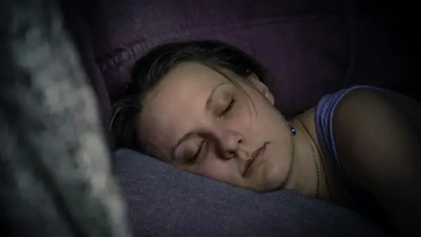 A woman lying awake in bed at night, phone glowing softly in dim light