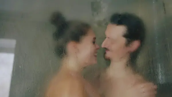 A woman and a man facing each other behind a wet glass shower door