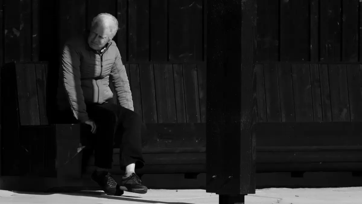 An elderly person sits alone on a bench.