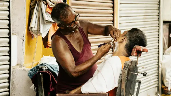 Barber shaves a customer's face with razor.