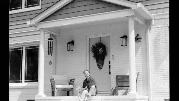 Person sitting on front porch steps of a house.
