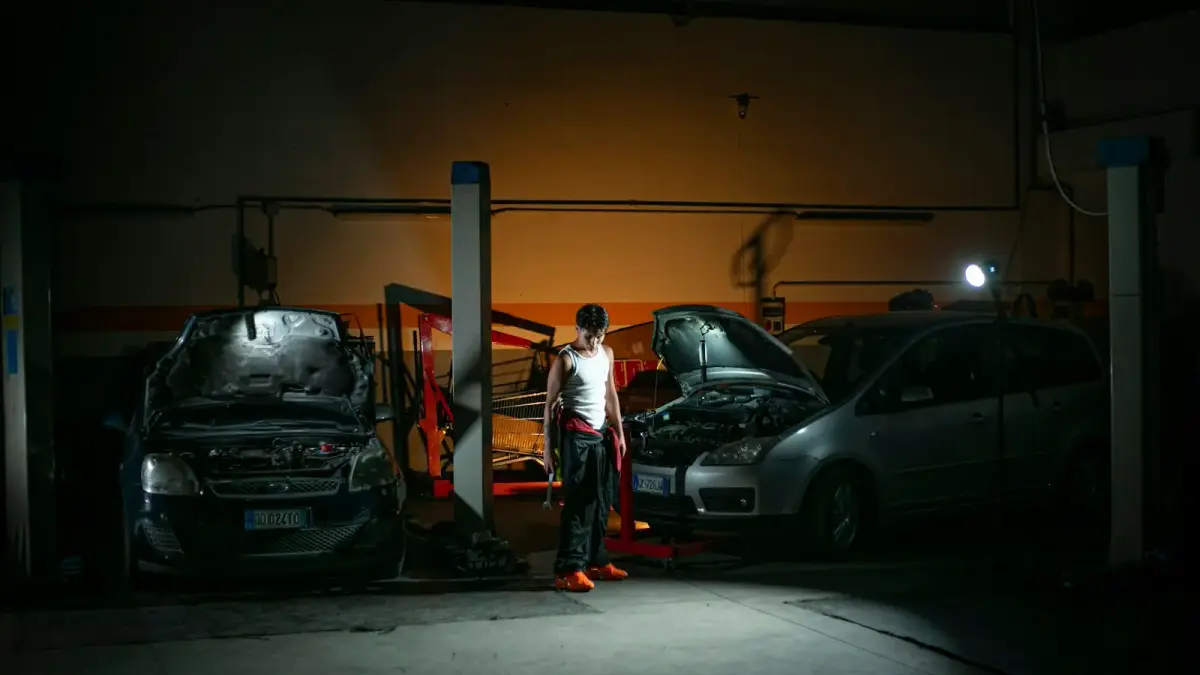 Mechanic working on cars in a dimly lit garage.