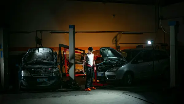 Mechanic working on cars in a dimly lit garage.